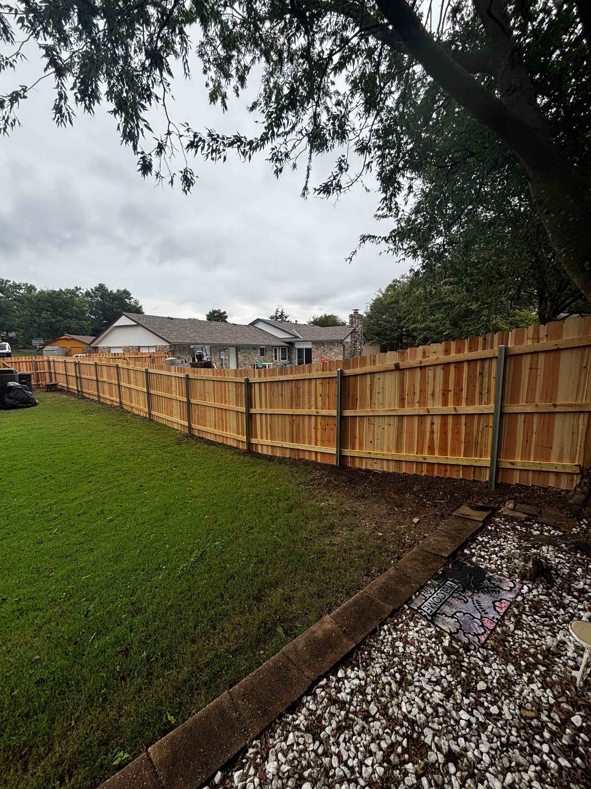 Backyard with a new wooden fence along a grassy lawn under cloudy skies