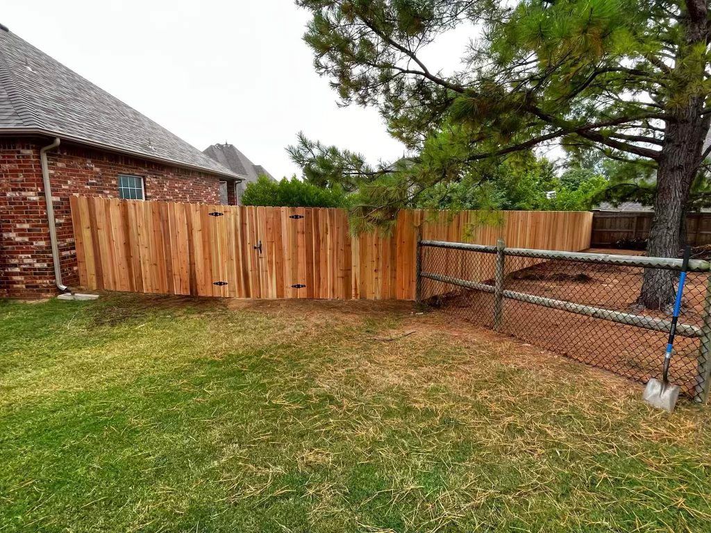 Backyard with a wooden fence, brick house, tree, and chain-link enclosure on a grassy lawn
