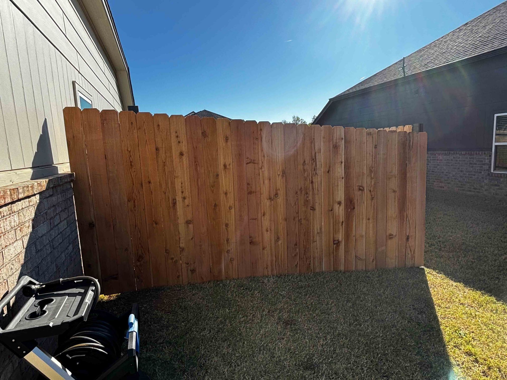 Backyard with a tall wooden fence between two houses under a bright blue sky