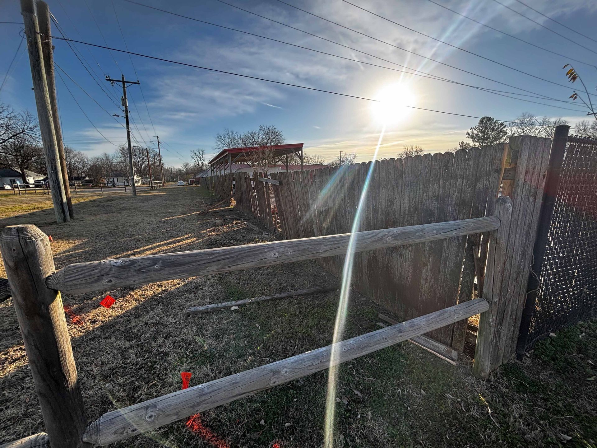 Snow-dusted wooden fence at sunrise with bright sun flare over a rural yard