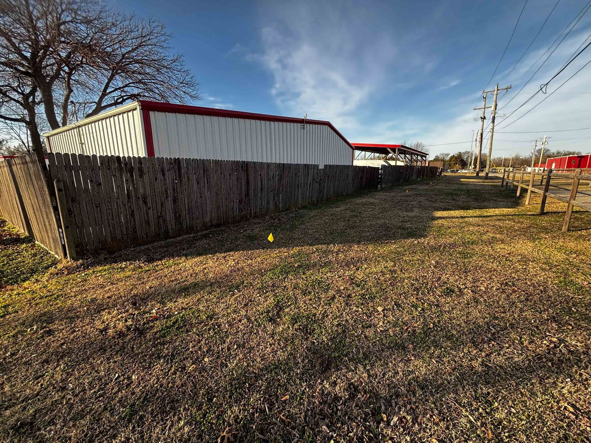 Fenced grassy lot beside a white building with red trim under a clear blue sky