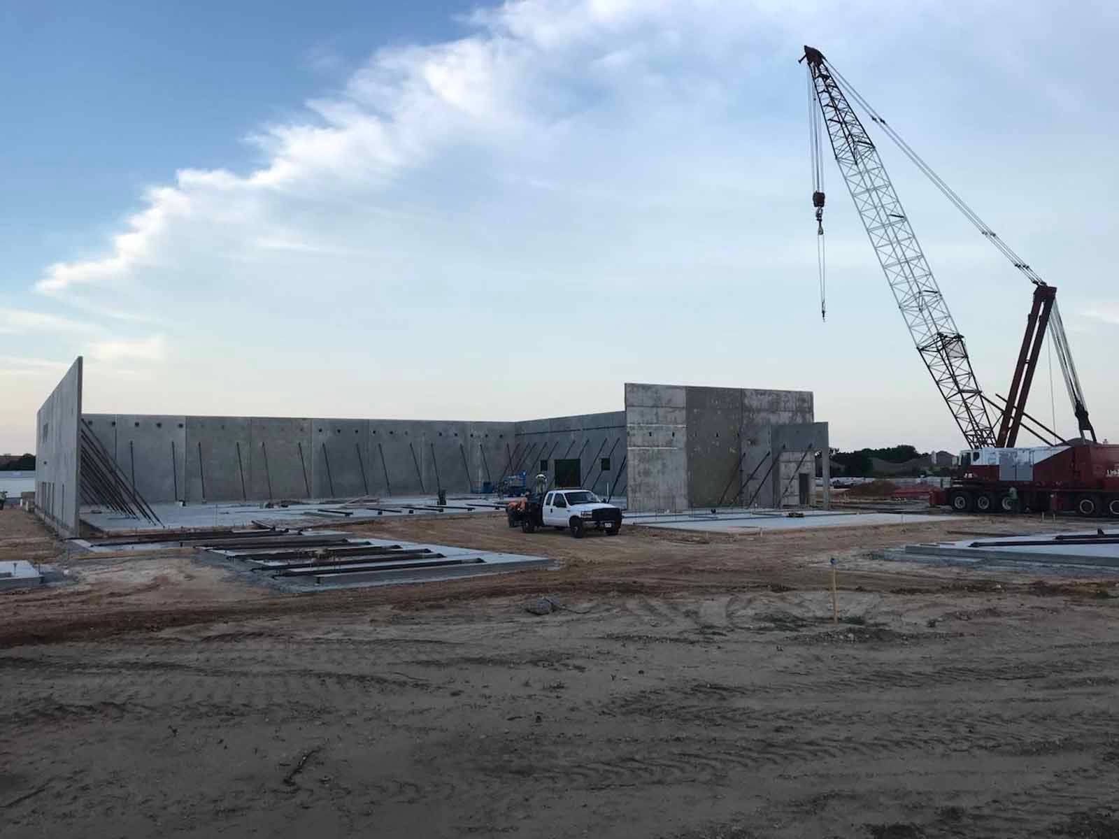 Construction site with concrete walls, a crane, and a white truck under a clear sky