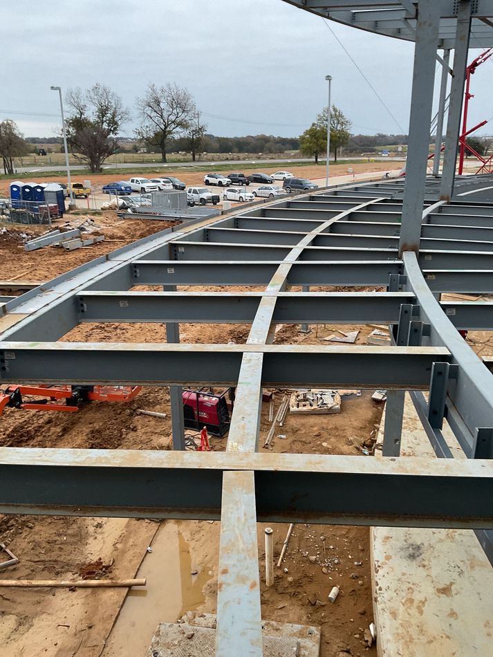 Steel frame building under construction with roof trusses and stairs on a sandy site