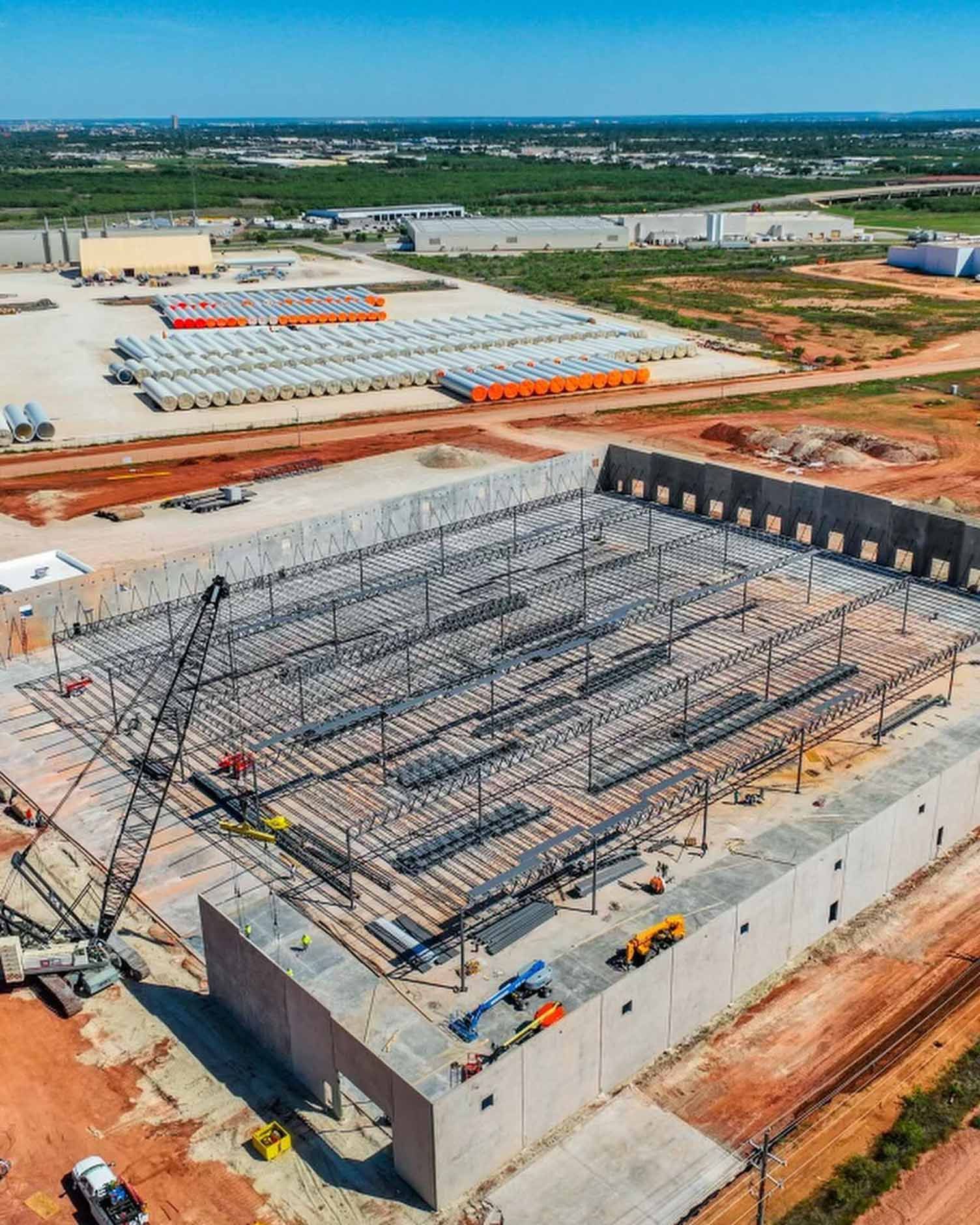 Aerial view of a large construction site with concrete walls, steel framework, and stacked materials