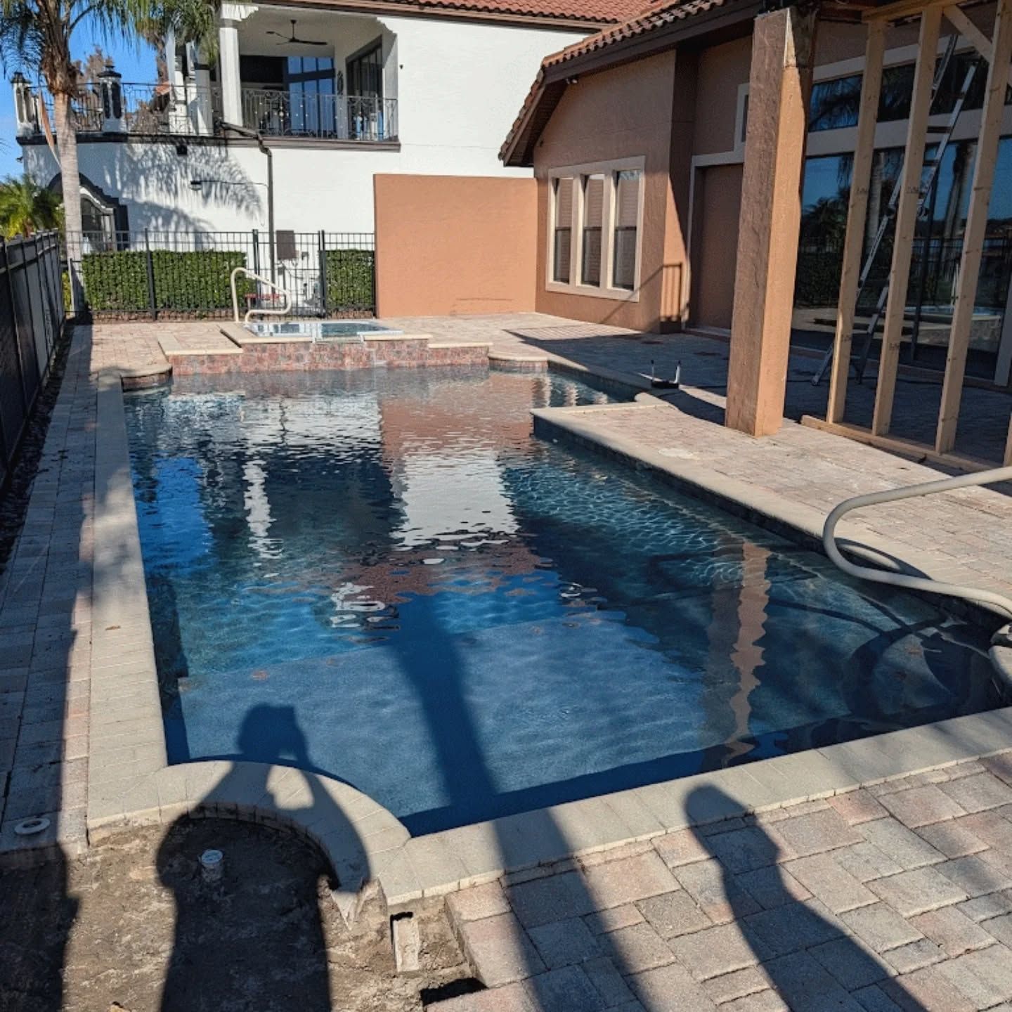 Screened backyard pool with hot tub, blue water, and paved deck in sunlight