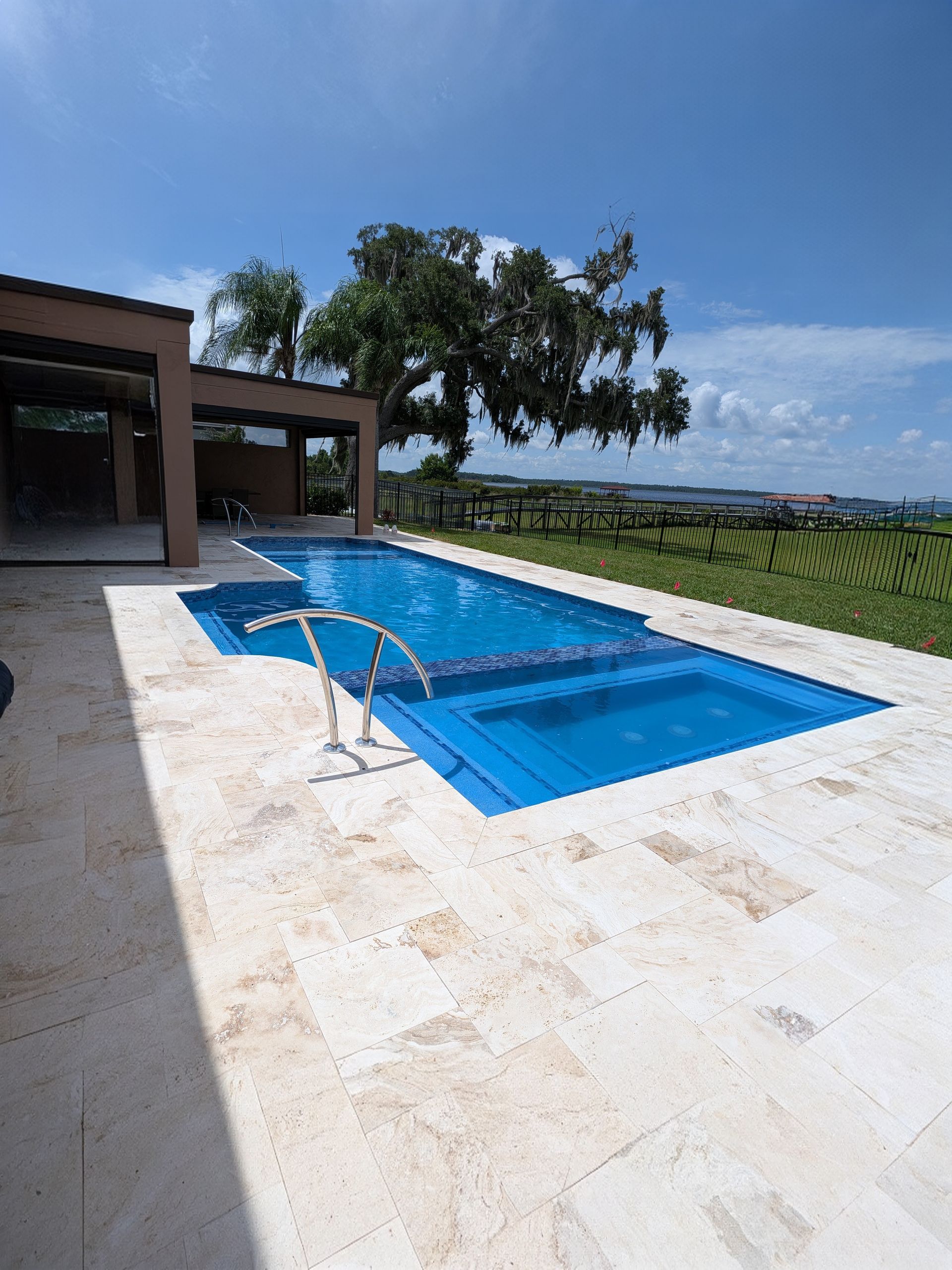 Modern backyard with a blue rectangular swimming pool beside a patio and grassy landscape.
