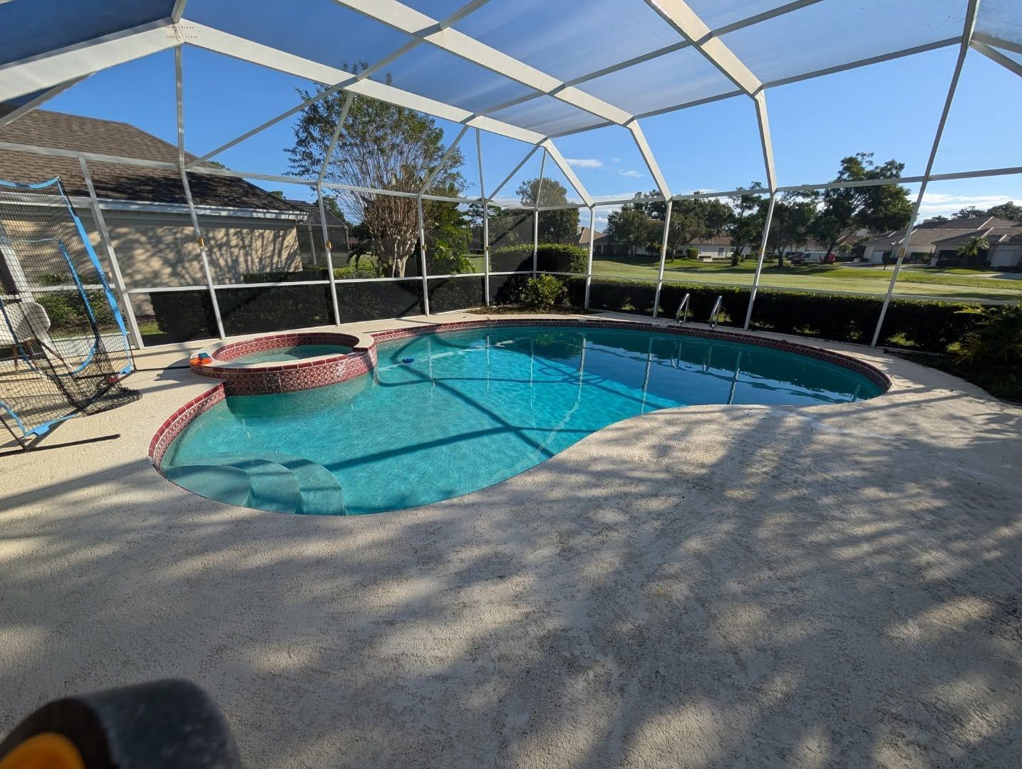 Screened backyard pool with hot tub, blue water, and paved deck in sunlight