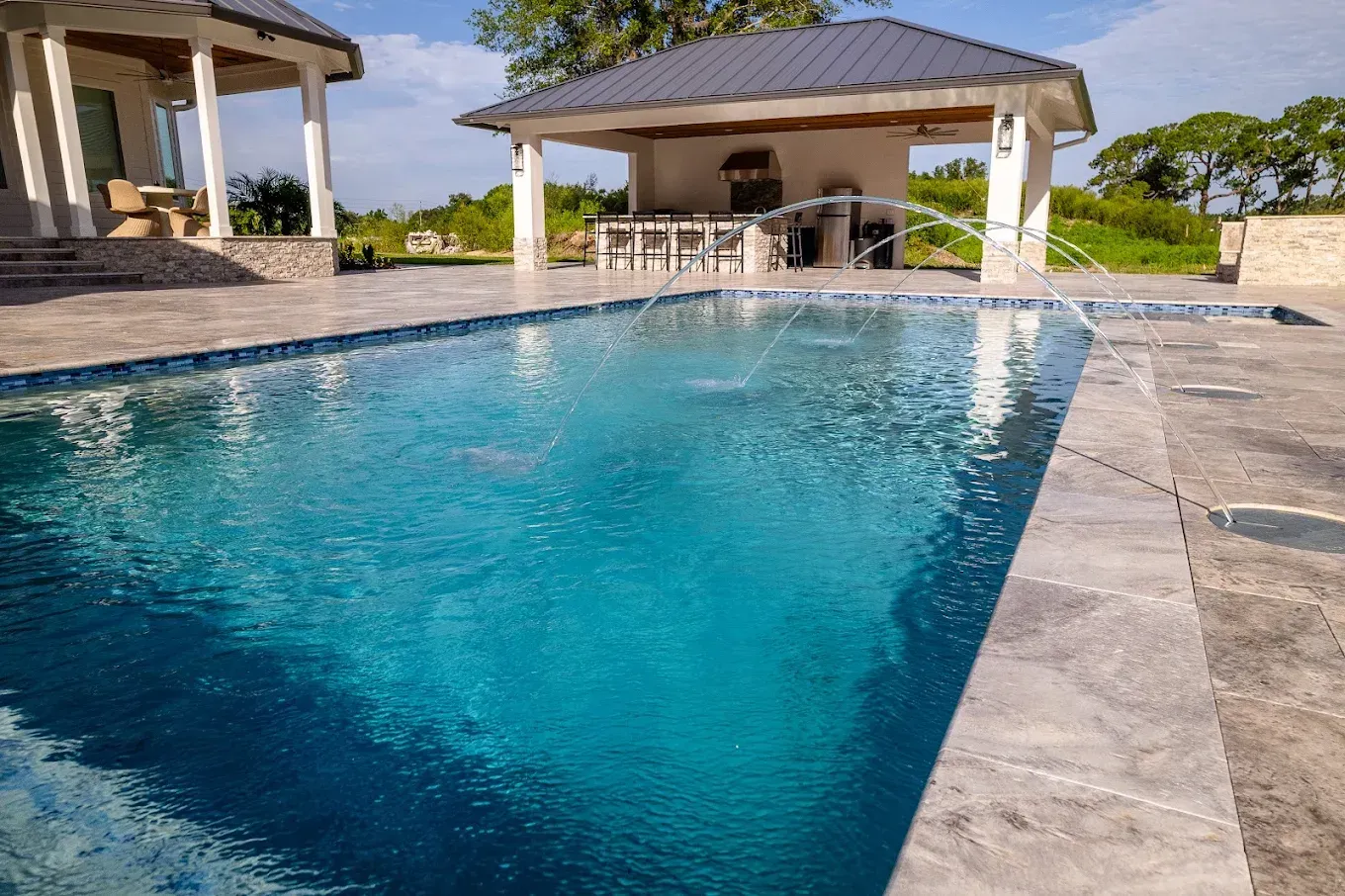 Blue swimming pool beside a stone patio and covered outdoor pavilion under a sunny sky