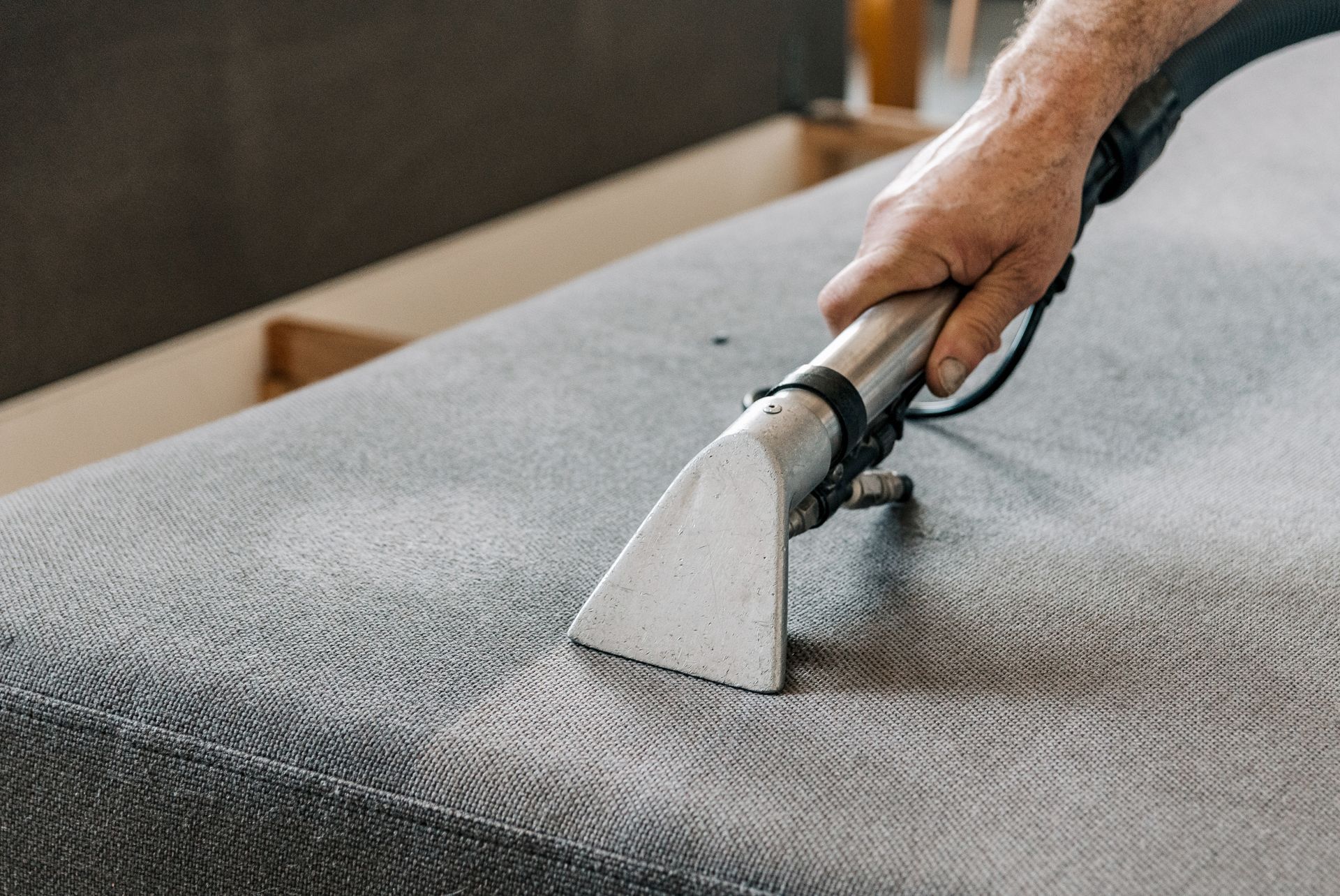 A person is cleaning a couch with a vacuum cleaner.