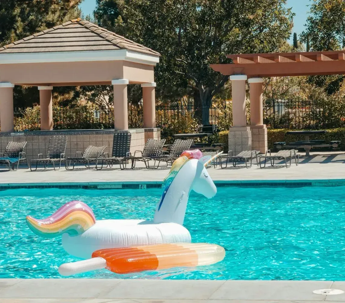 Unicorn pool float in a bright outdoor swimming pool with cabanas and lounge chairs behind it