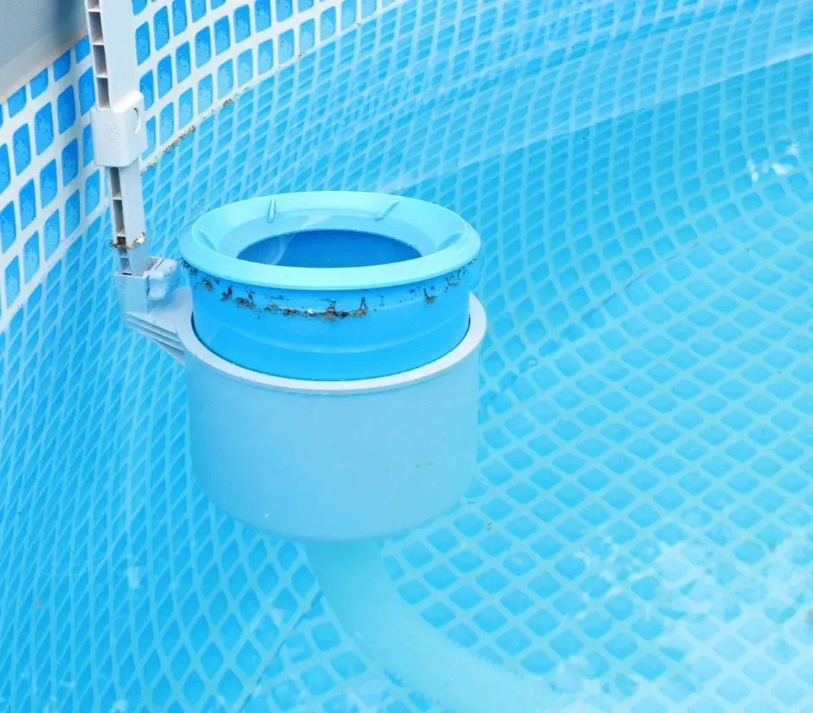 Blue pool skimmer bucket floating in a tiled swimming pool with a hose attached