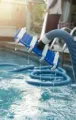 Pool vacuum cleaning a blue-tiled swimming pool with sunlight reflecting on the water
