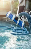 Pool vacuum cleaning a blue-tiled swimming pool with sunlight reflecting on the water