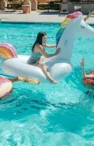 People floating on unicorn and rainbow pool inflatables in a sunny swimming pool
