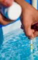 Hand holding a test strip over blue pool water, checking the water quality