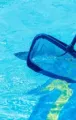 Pool skimmer net in blue water beside the pool edge