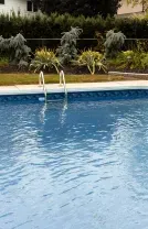 Blue swimming pool with two fountain jets and landscaped greenery in the background