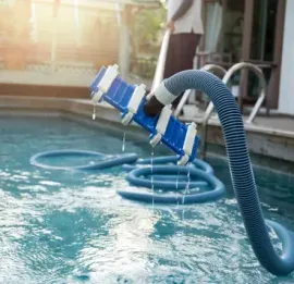 Pool vacuum cleaning a blue-tiled swimming pool with sunlight reflecting on the water