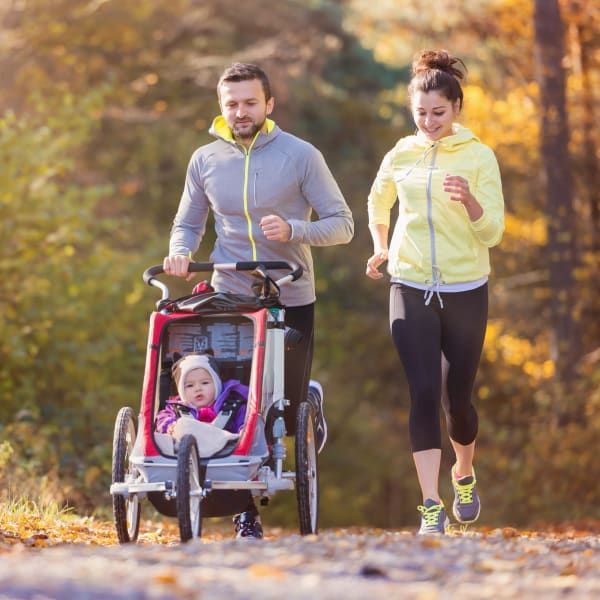 Couple jogging with baby in stroller on a path through autumn trees.