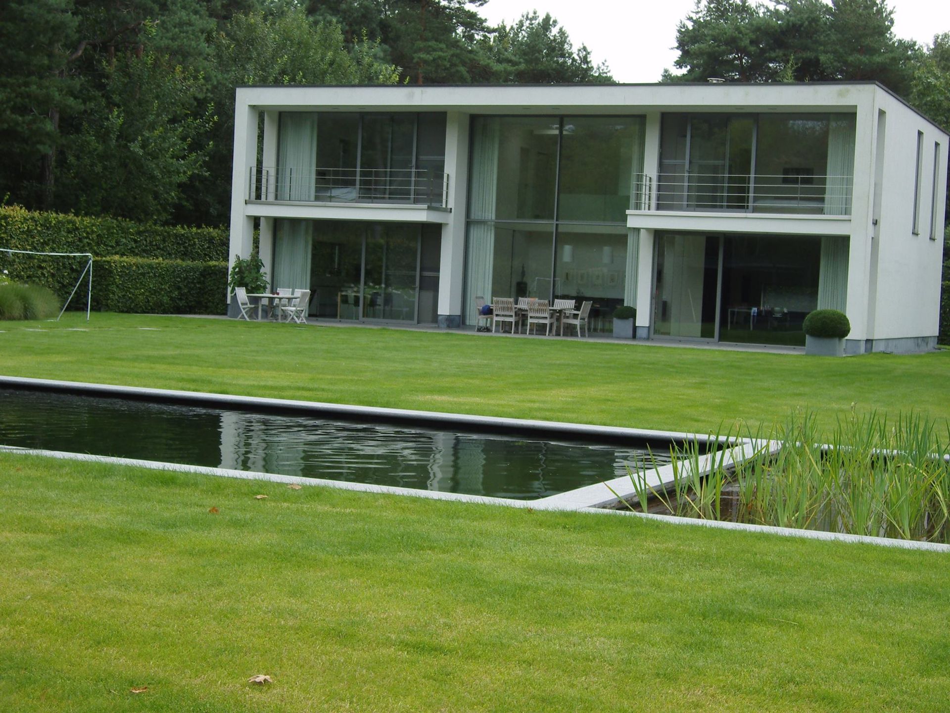 Een huis met een groot gazon en een vijver ervoor, Bio pools & gardens