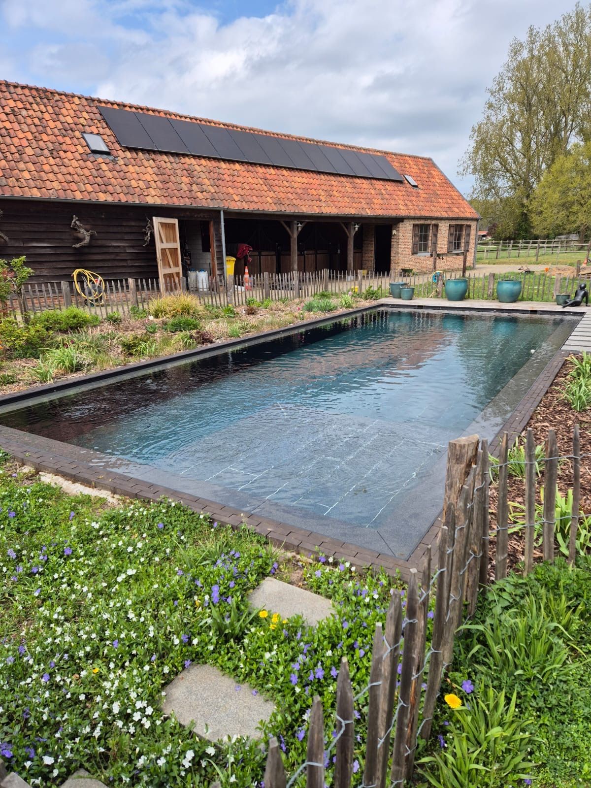 Rustieke boerderij met een rechthoekig zwembad en tuin op de voorgrond.