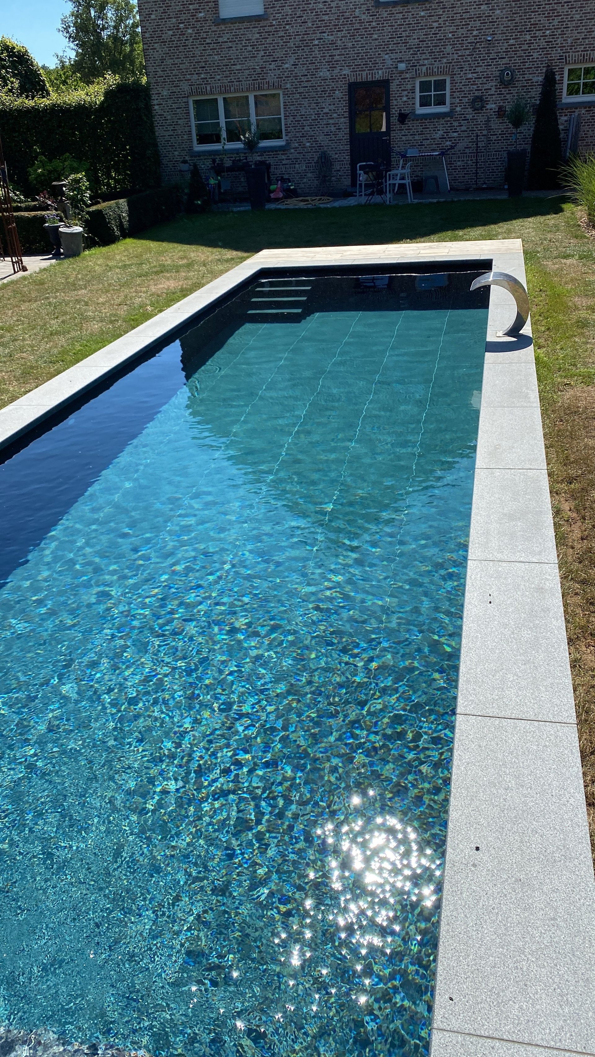 Zwembad in de achtertuin met blauw water en een stenen terras naast een huis.
