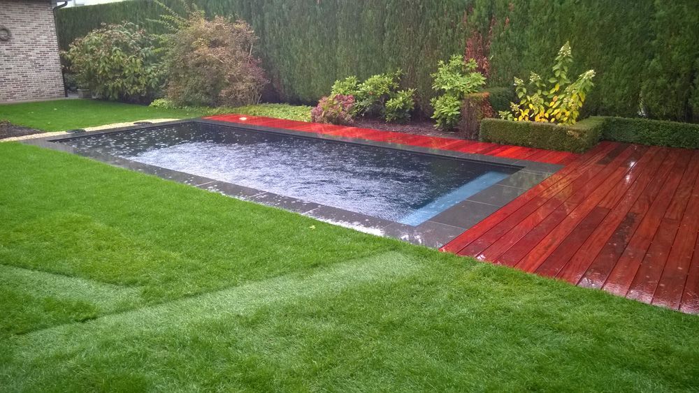 Een zwembad omgeven door een houten dek en een weelderig groen gazon.