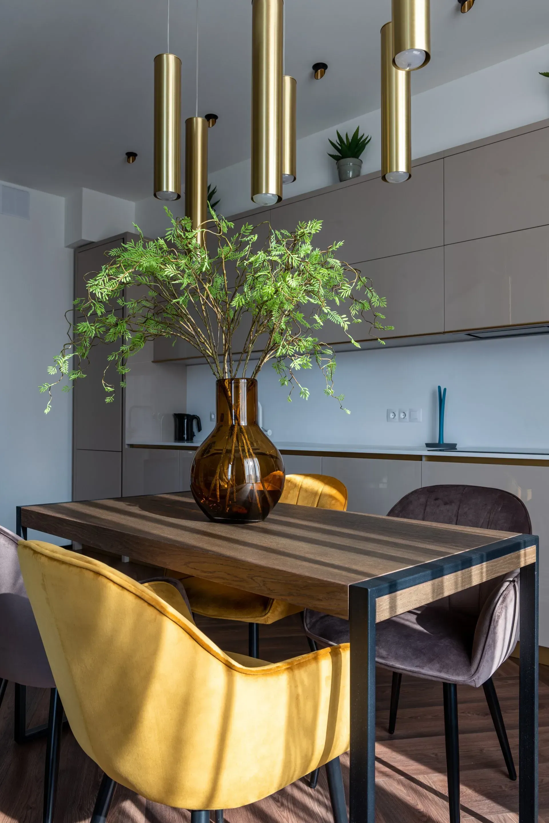 Dining area with a wooden table, yellow and gray chairs, and a vase of greenery.