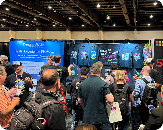 Crowd at a conference booth with shirts on display, blue DynamicWeb backdrop. People browsing, talking, and looking.
