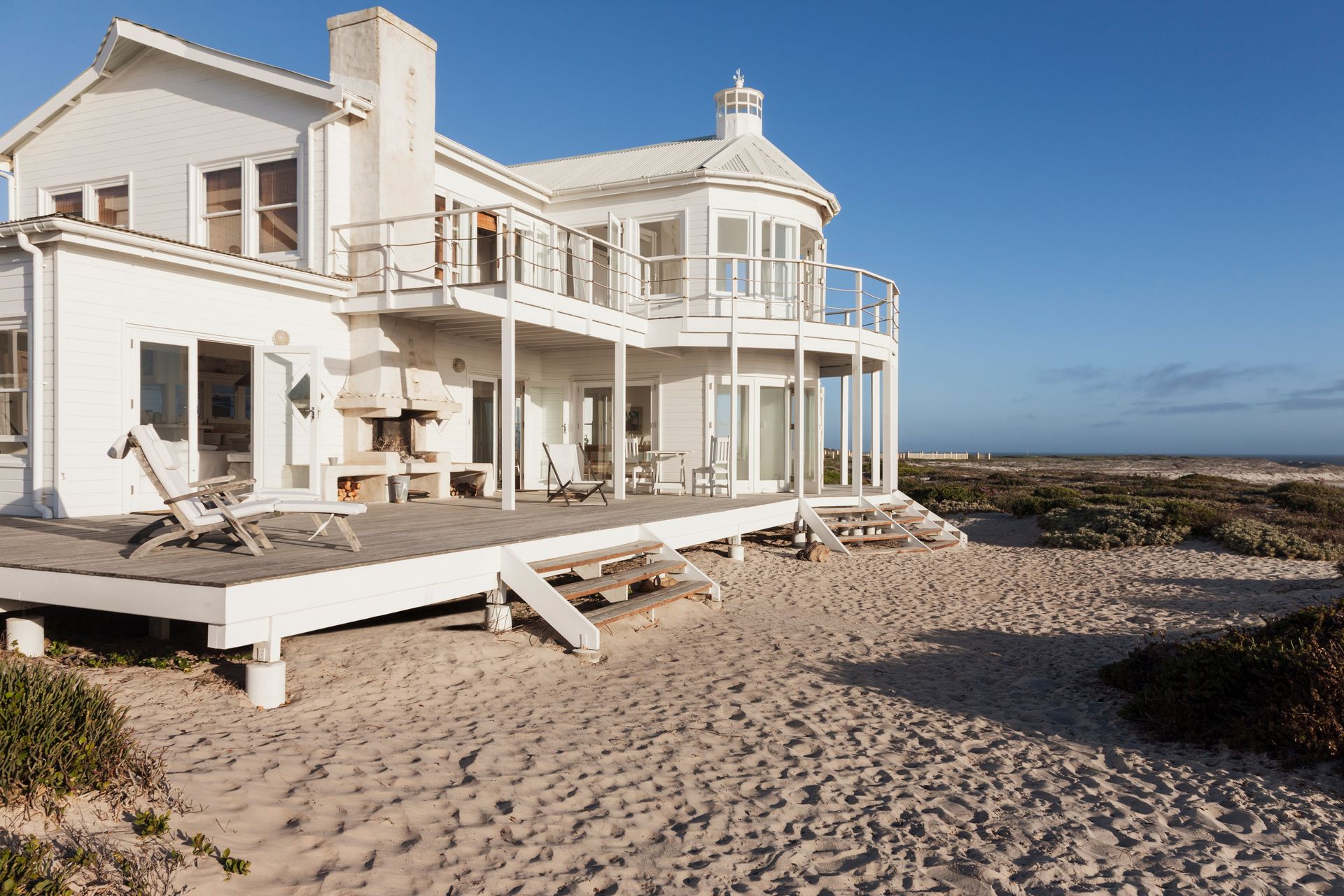 A large white house is sitting on top of a sandy beach.