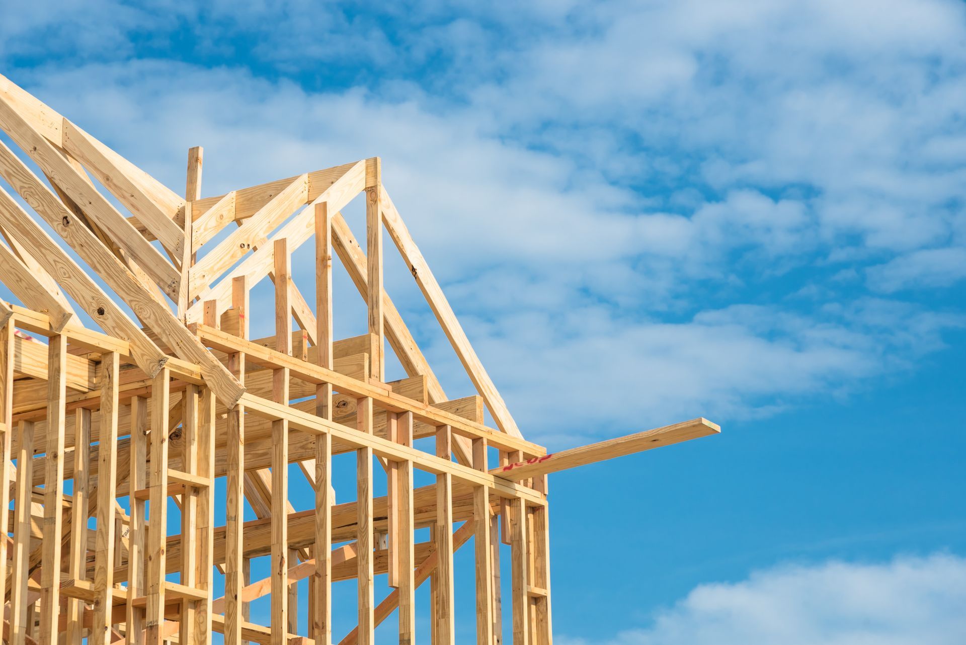 Wooden framework of a house under construction against a bright blue sky with white clouds.