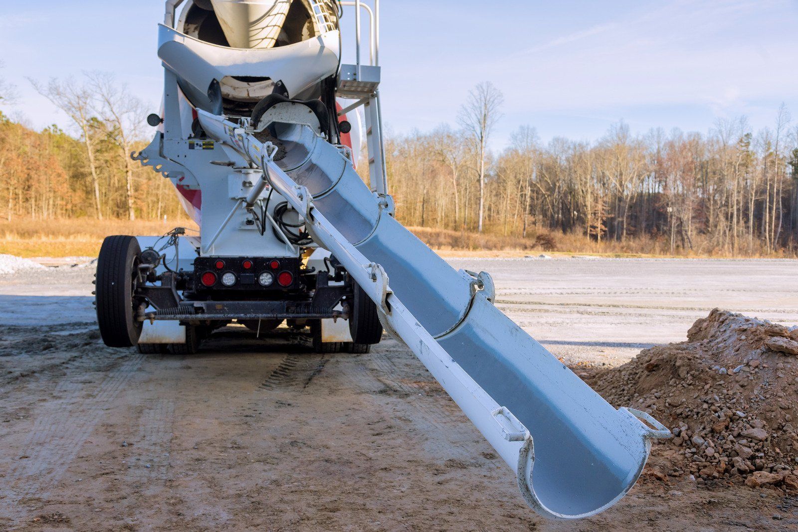 Concrete mixer truck with chute extended over a gravel lot in a wintery outdoor setting