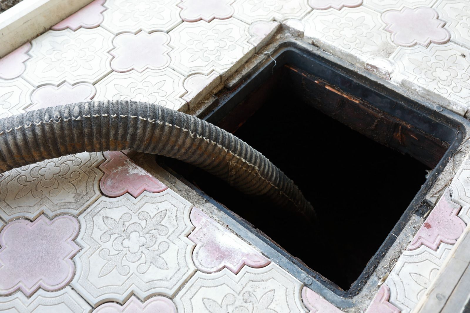 Corrugated hose entering a dark square opening in a patterned tiled floor