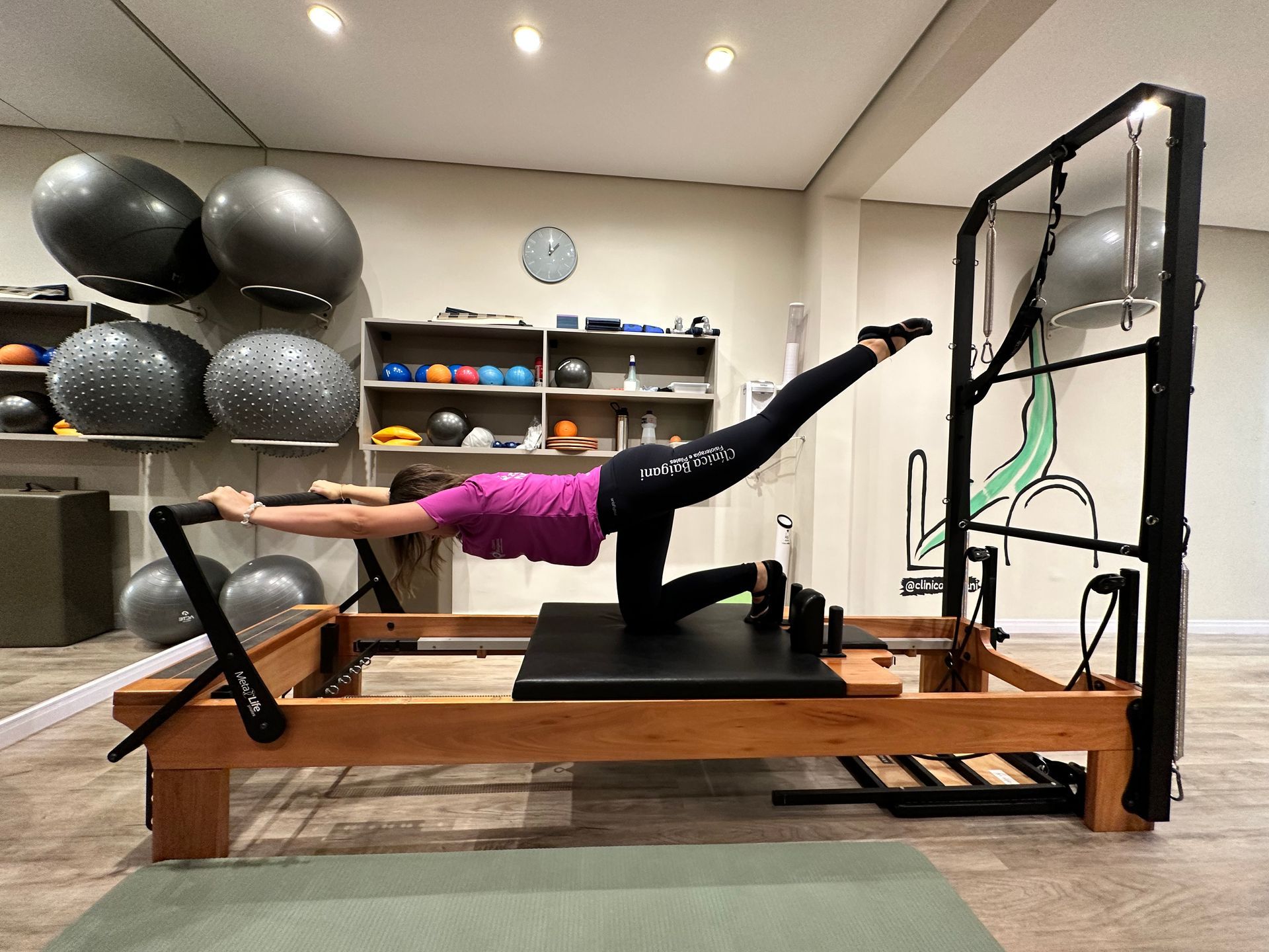 Pessoa em equilíbrio em um aparelho de Pilates Reformer em uma academia, estendendo um braço e uma perna.