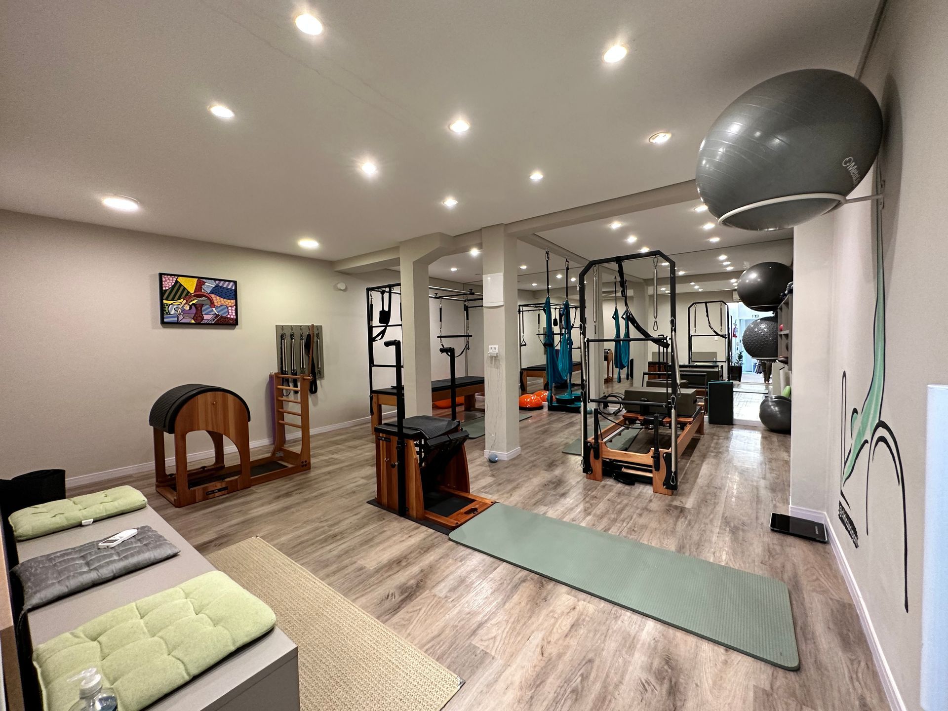 Academia residencial bem iluminada com equipamentos de ginástica, TV de parede, colchonetes e luzes embutidas no teto.