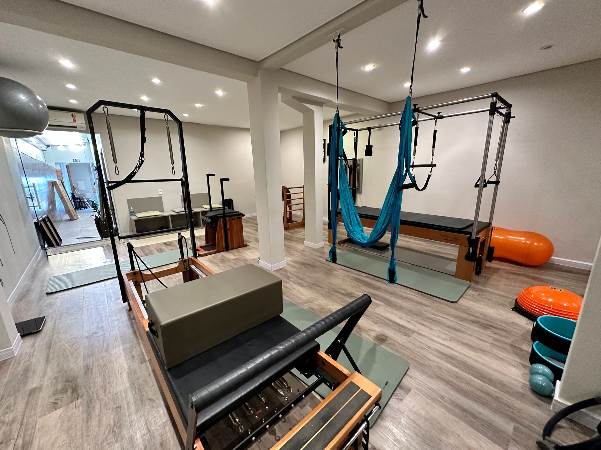 Estúdio de Pilates com aparelhos Reformer, faixas de suspensão e equipamentos de ginástica em uma sala bem iluminada.