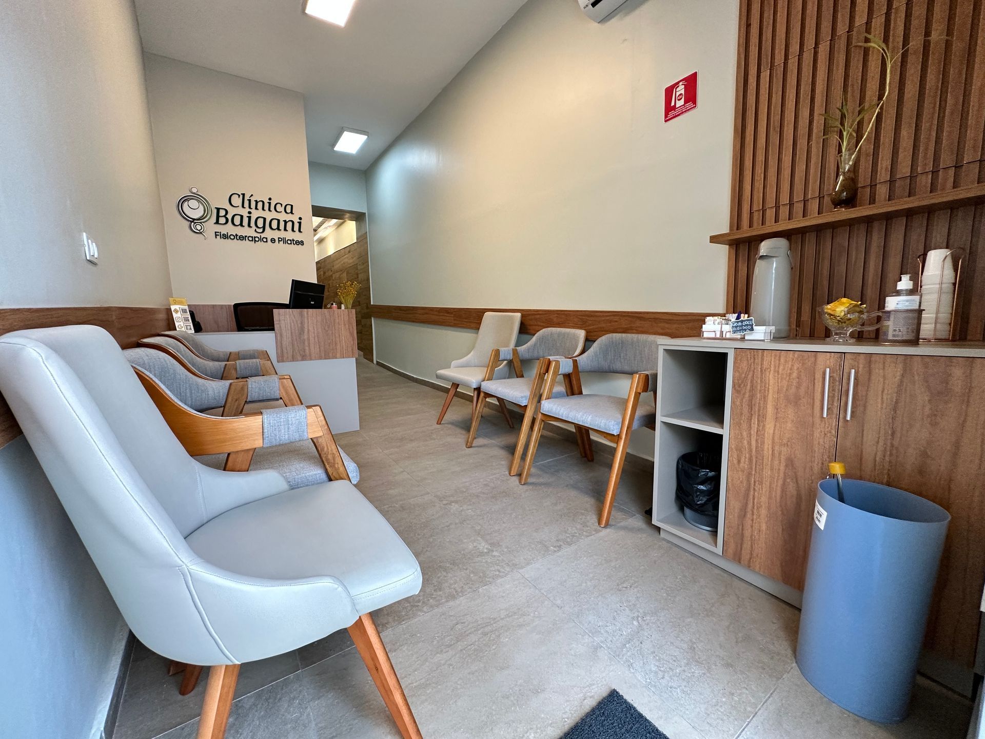 Sala de espera moderna com cadeiras azul-claras, detalhes em madeira e um espaço para preparo de café.