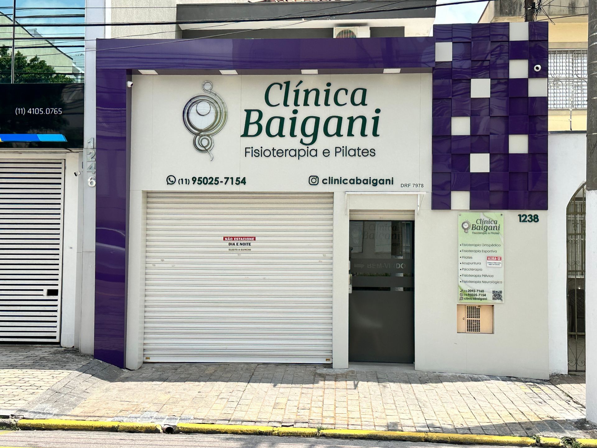 Fachada da Clínica Baigani com vitrine branca e roxa e porta de metal fechada.