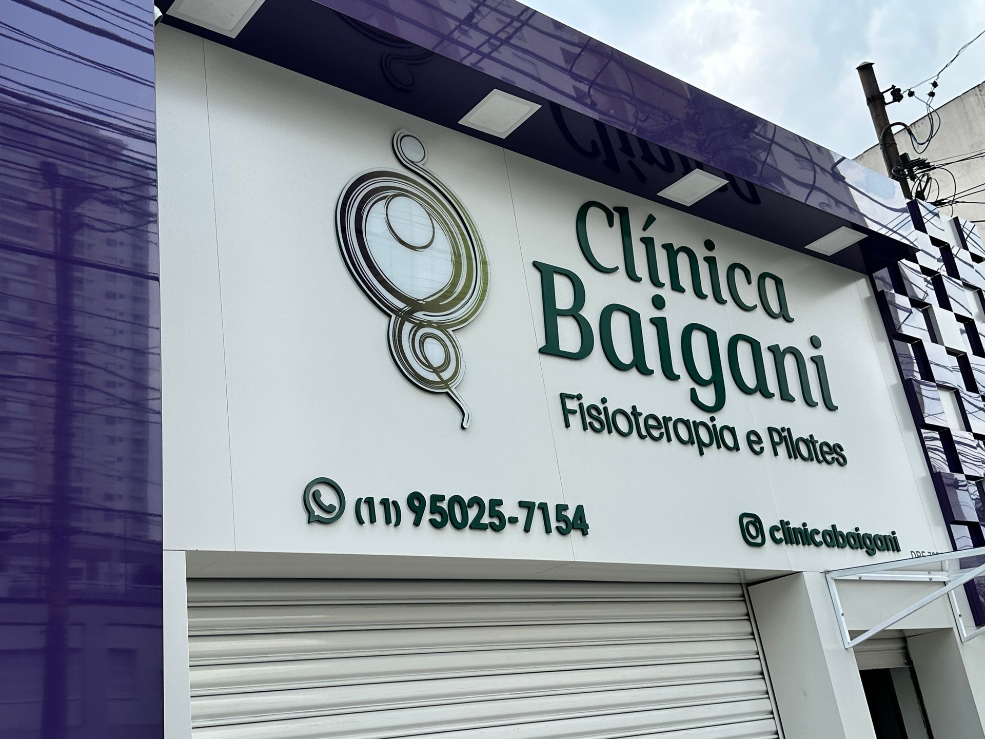 Placa da Clínica Baigani, especializada em fisioterapia e podologia, em um prédio branco e roxo.