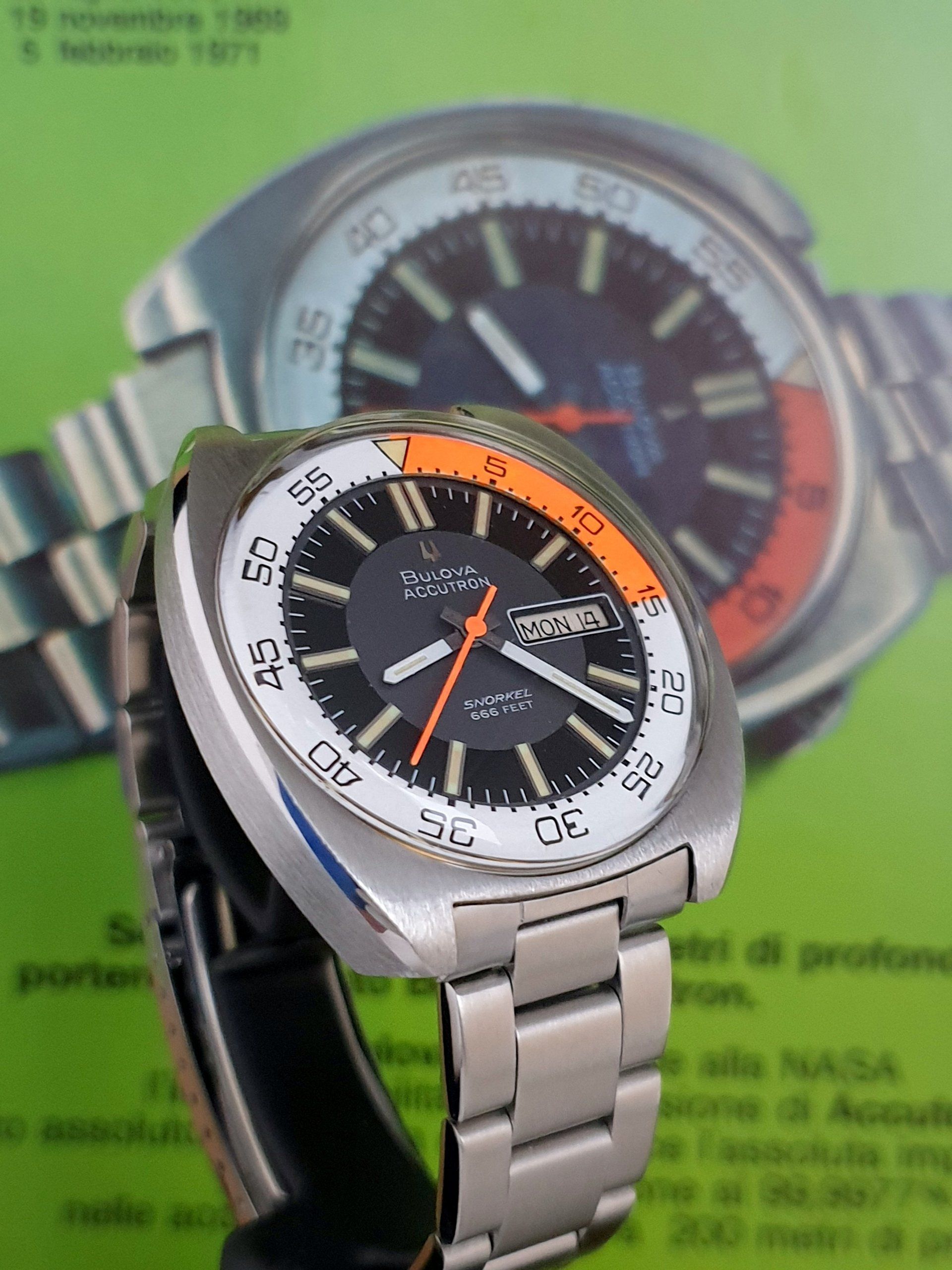 Two silver wristwatches with black faces, one in front showing an orange accent and a black strap