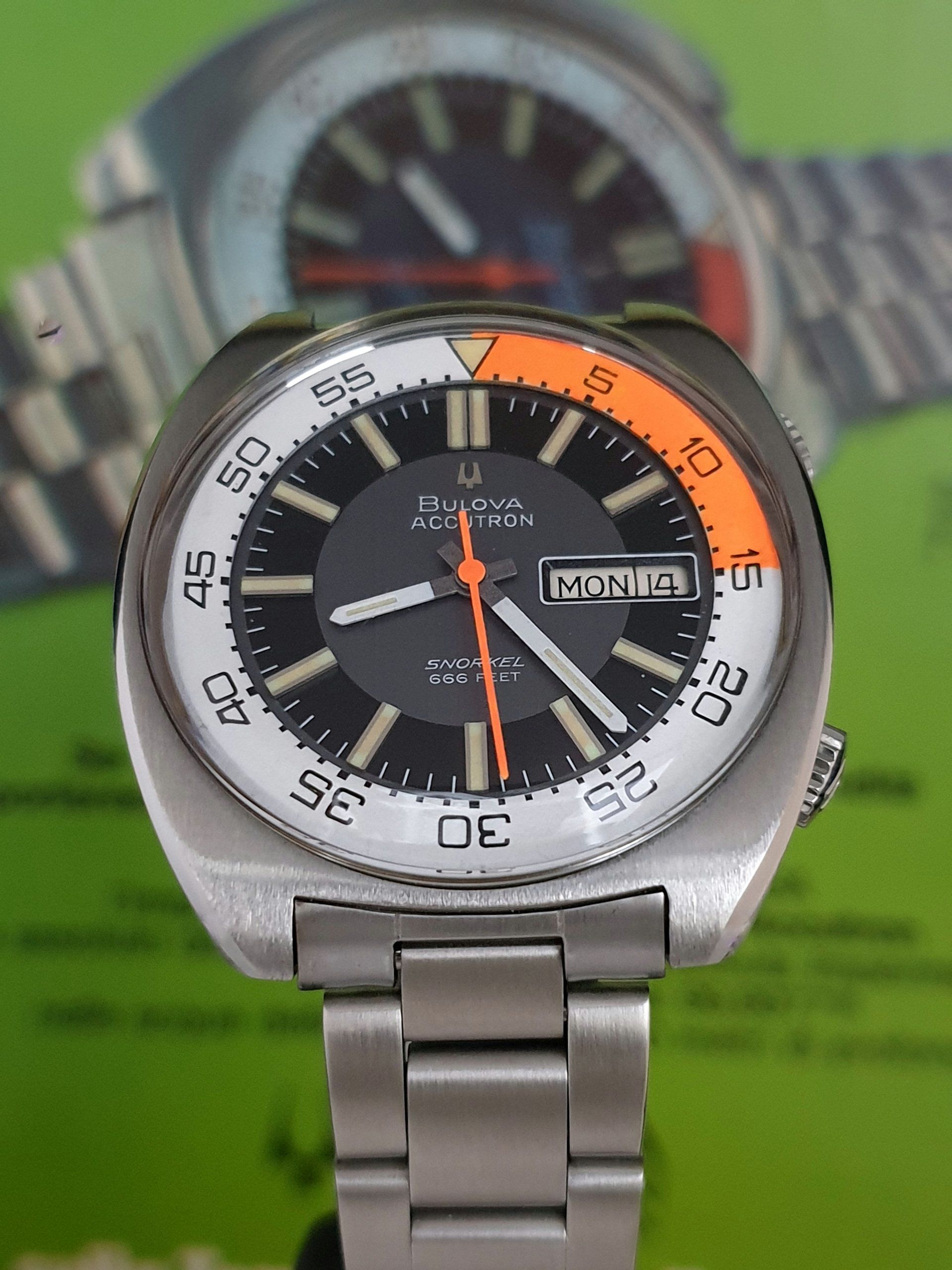 Close-up of a silver wristwatch with black dial and orange accents on a metal bracelet.