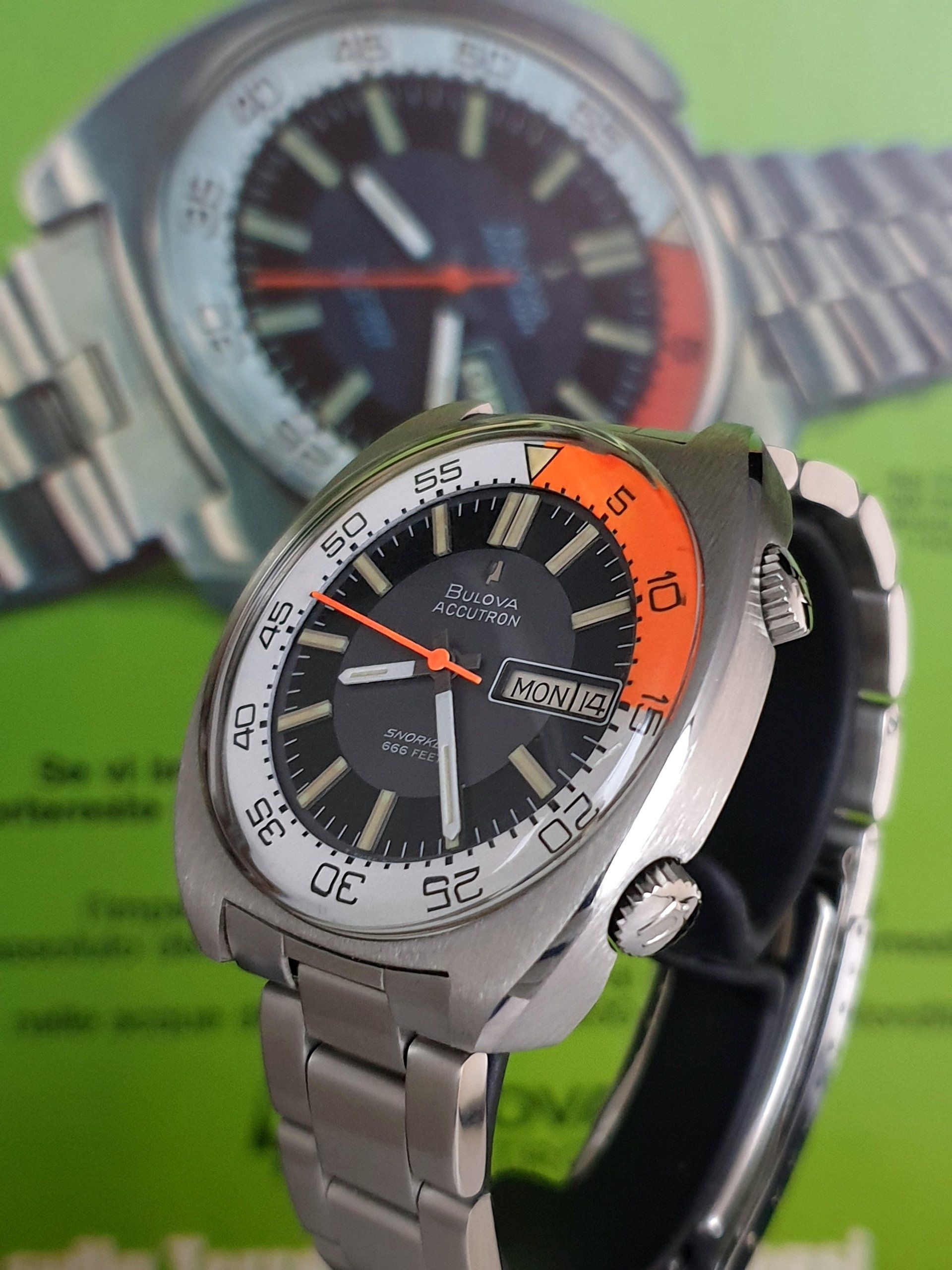 Two wristwatches, one silver with orange accents in front of a blurred watch in the background.