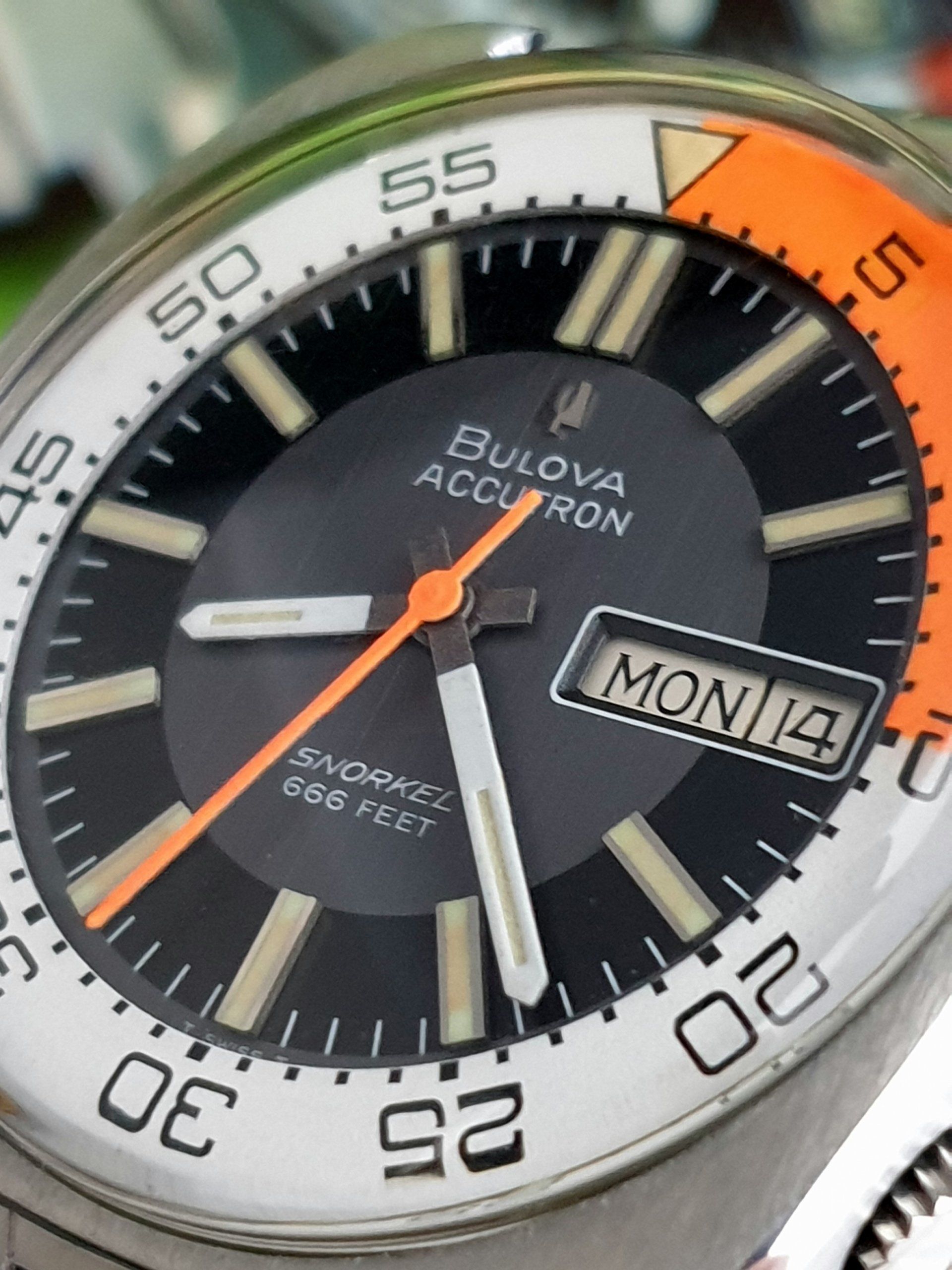 Bulova Accutron wristwatch with black dial, orange hand, and day-date display.