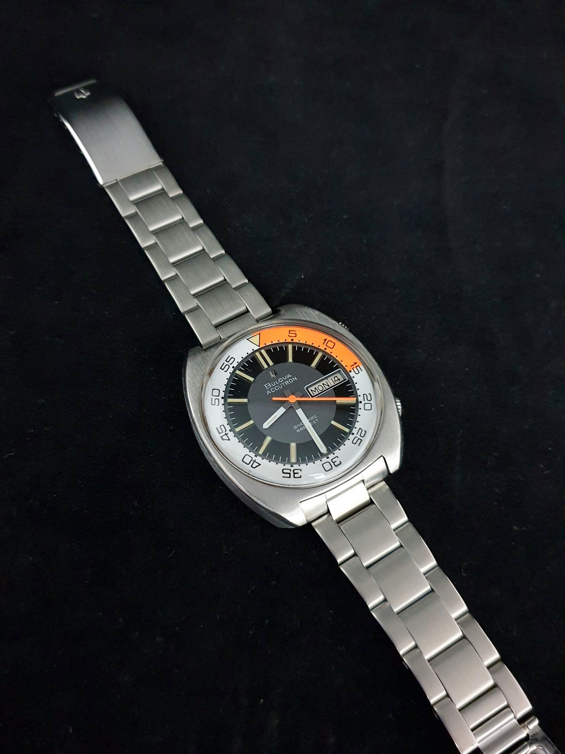 Silver wristwatch with black face and orange accent on a dark background