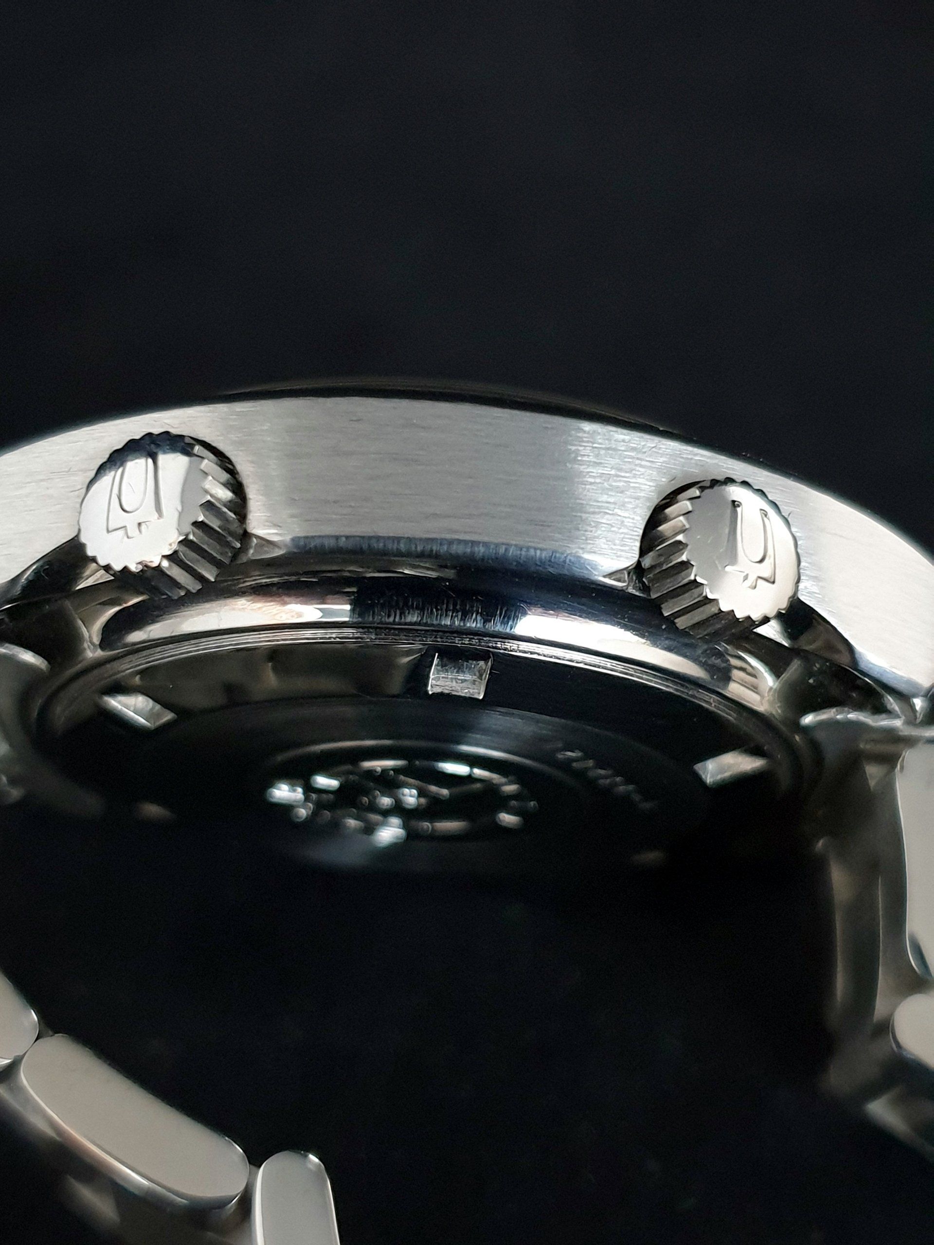Close-up of a silver wristwatch case with two crown buttons on a dark background