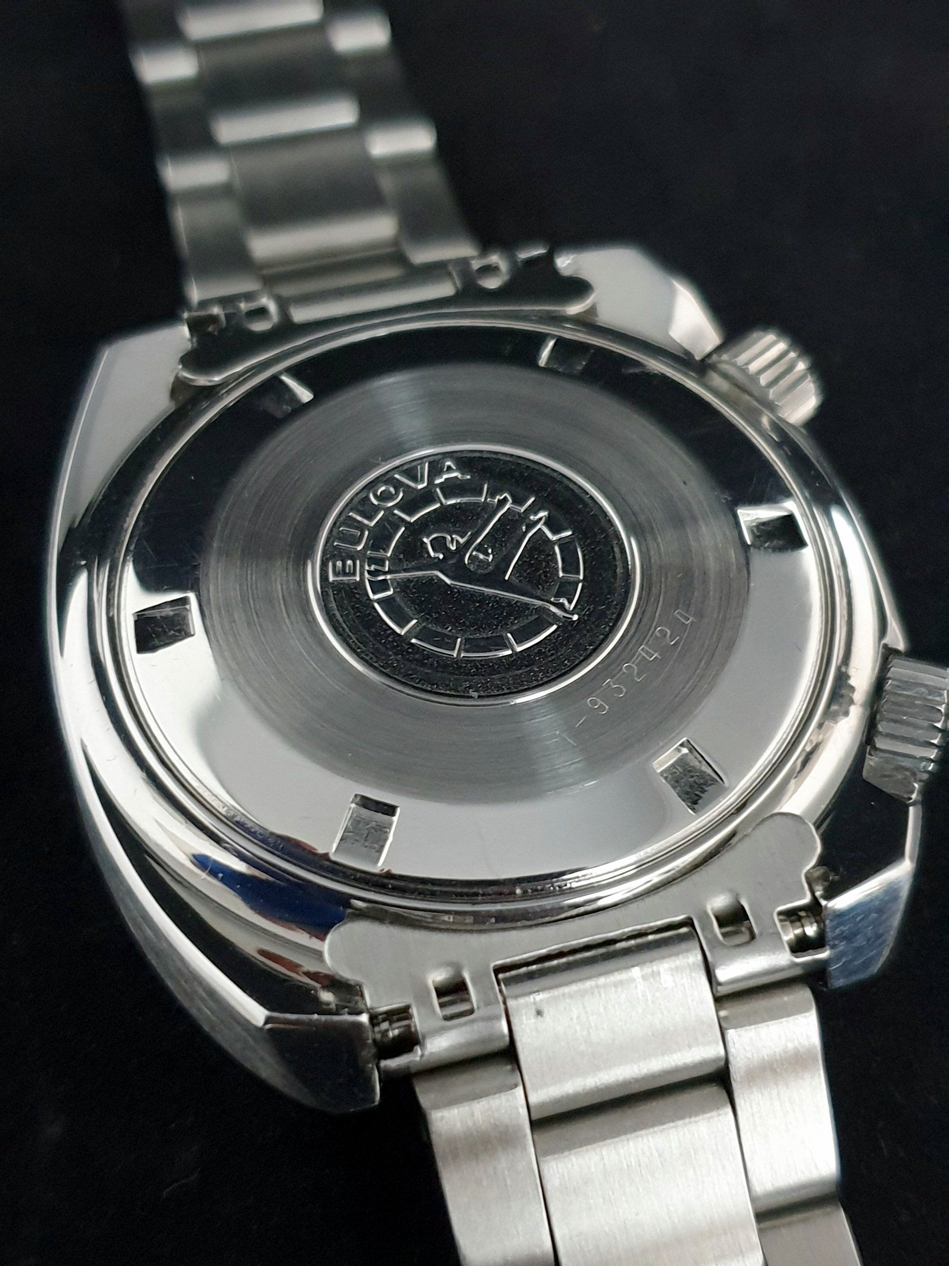 Close-up of a silver wristwatch back with metal band on a dark background