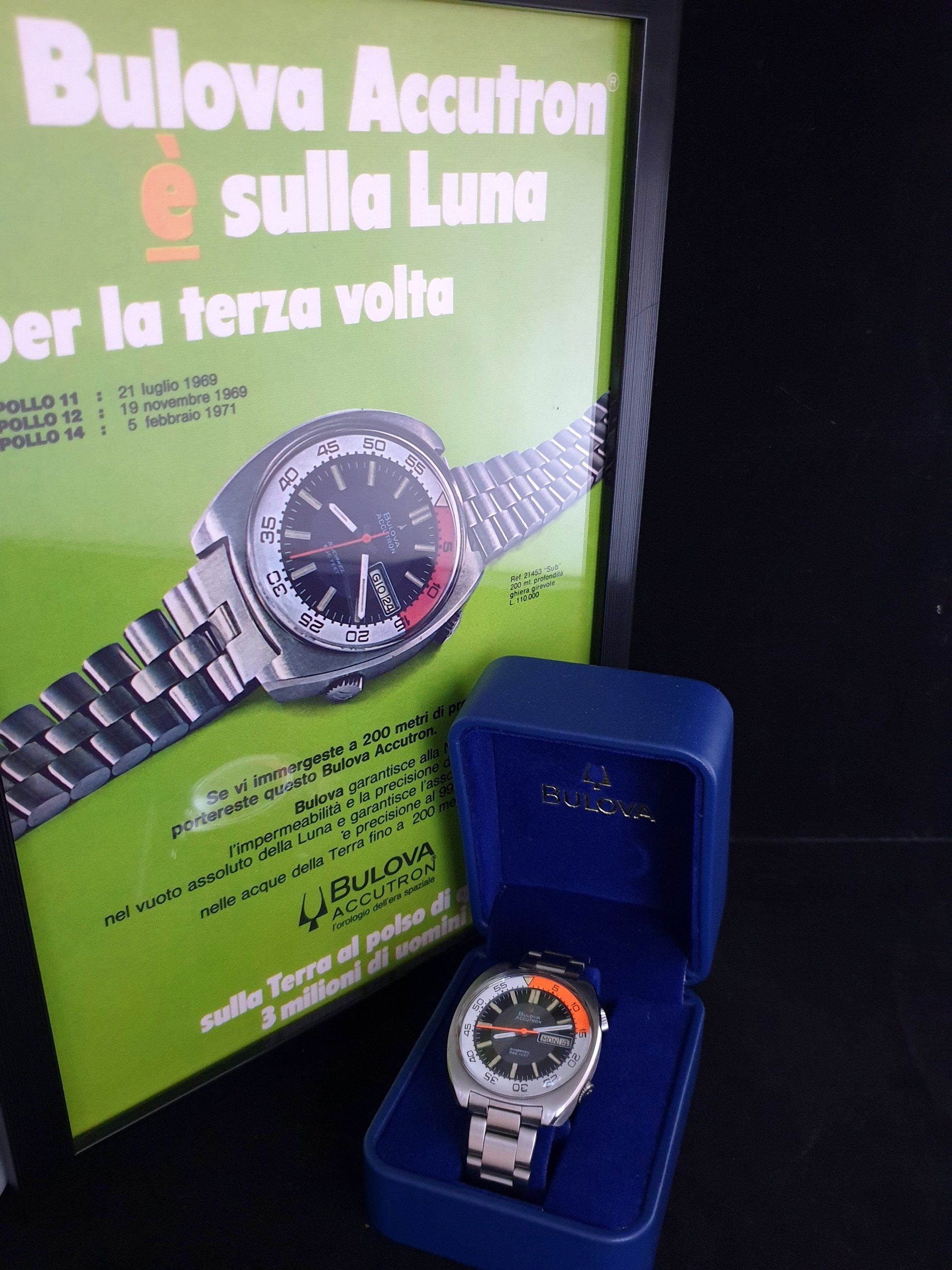 Bulova Accutron watch display with green poster and a silver watch in a blue box.