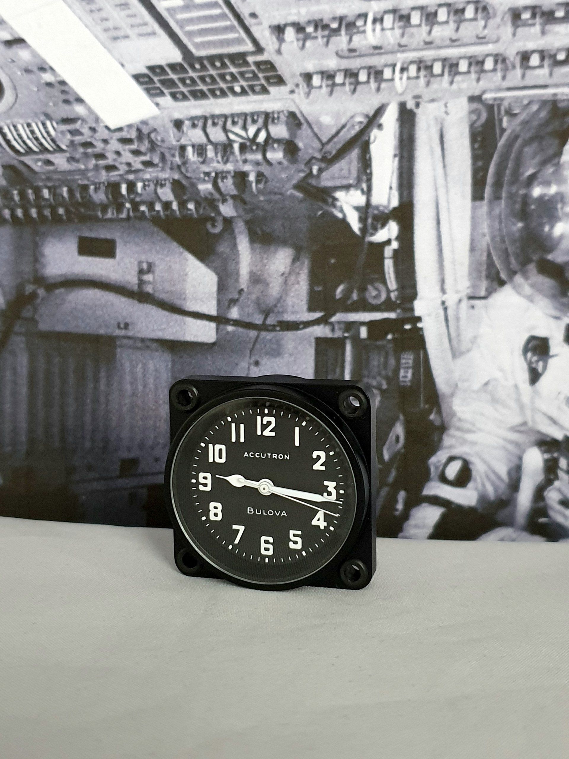 Black alarm clock on a table, with a grayscale spacecraft interior and astronaut in the background