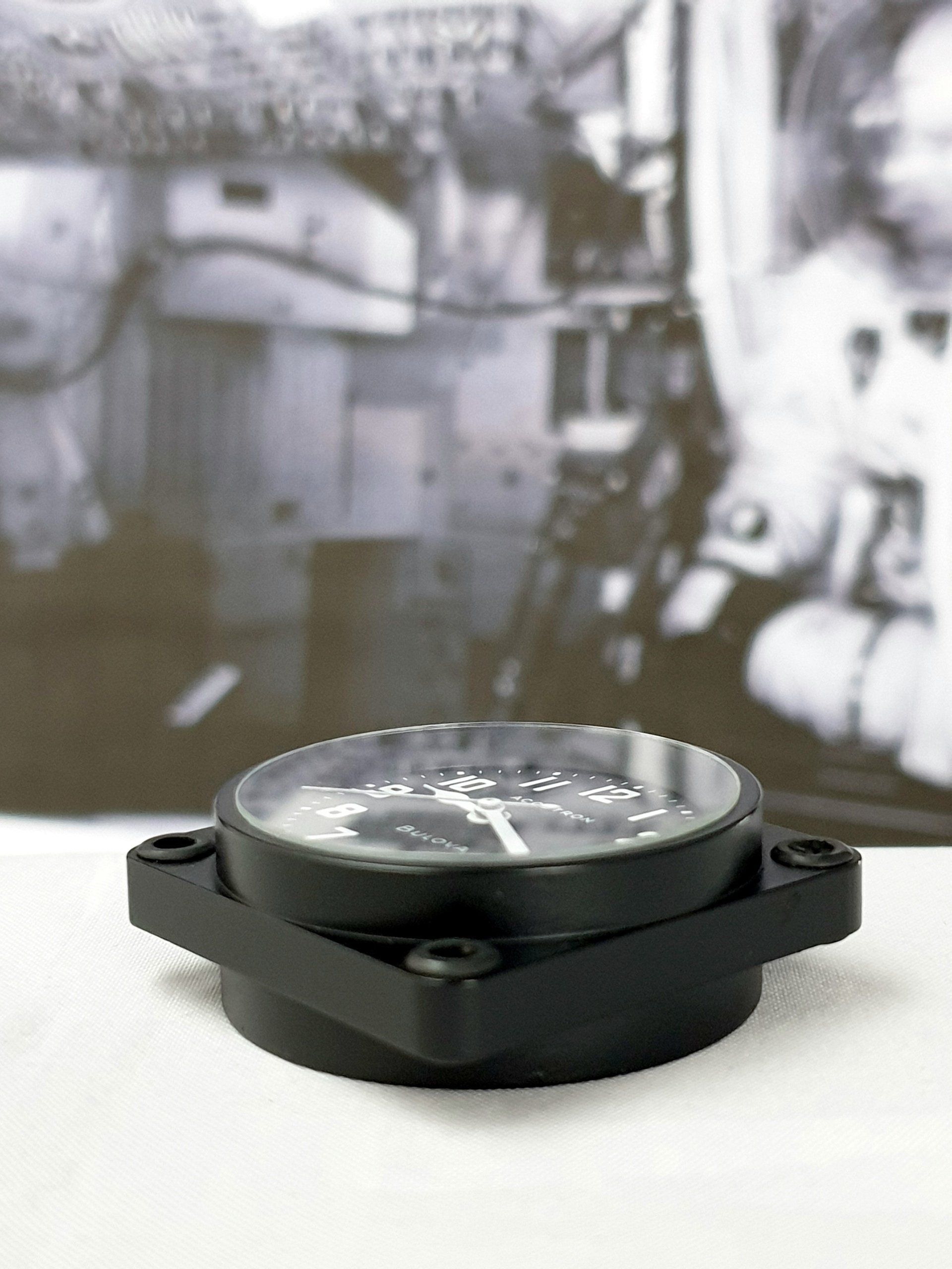 Black square wristwatch on a white surface with a blurred outdoor background