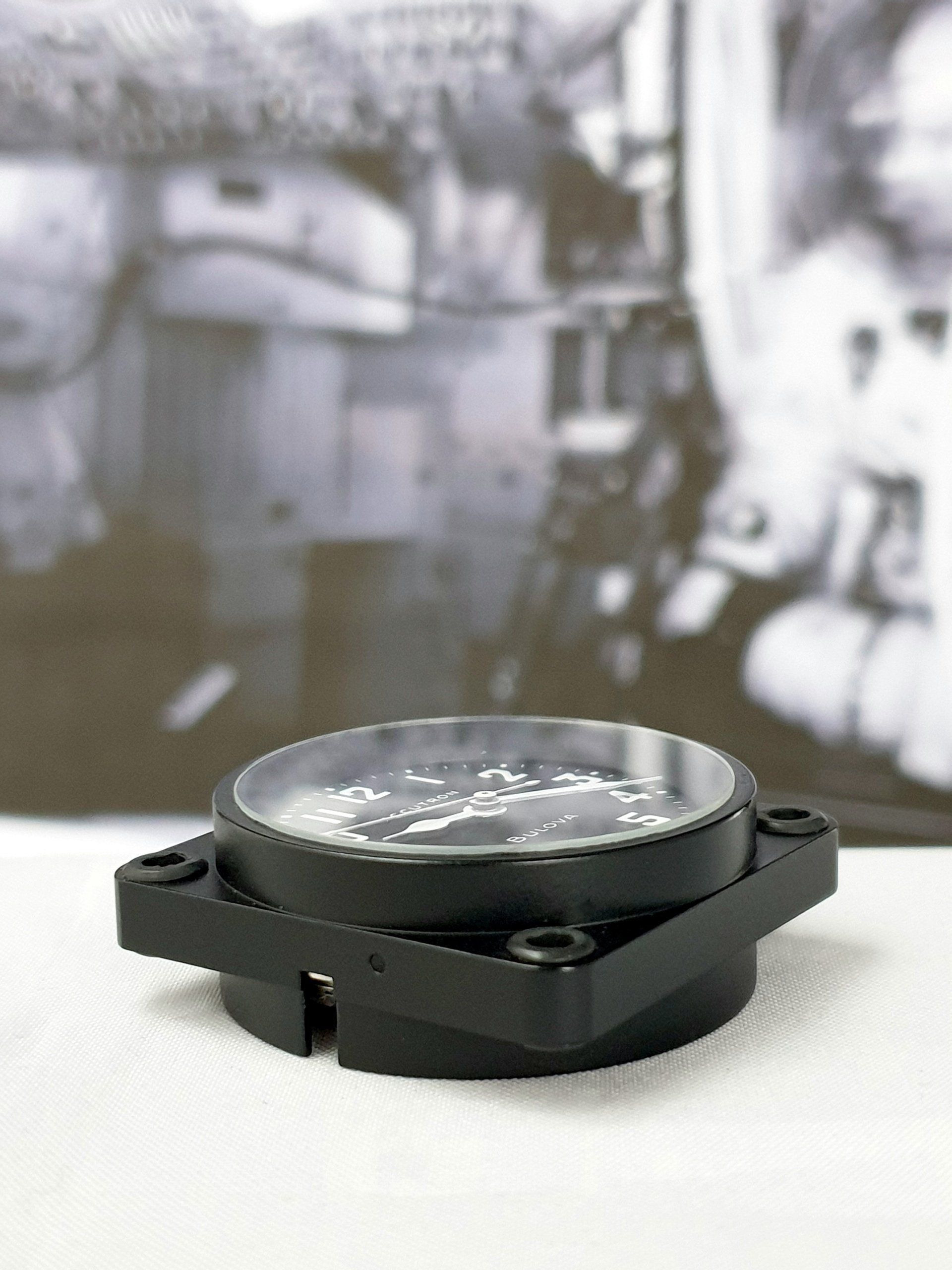 Black circular device with a clear top on a white surface, with a blurred industrial background
